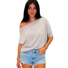 Woman wearing a taupe off-shoulder top and denim shorts on a white background