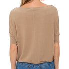 A woman viewed from the back wearing a loose, short-sleeve knit top in a warm tan or camel shade, paired with blue jeans against a plain white background.