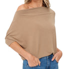 A woman wearing a beige off-the-shoulder knit top with three-quarter sleeves and blue jeans, shown from the neck down against a plain white background.