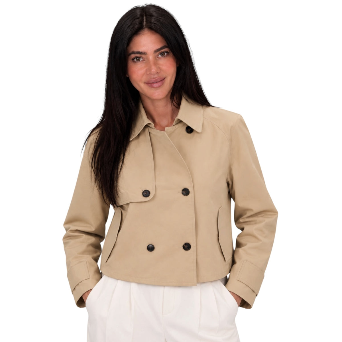A woman modeling a cropped beige double-breasted jacket with black buttons, paired with white trousers, against a solid white background.