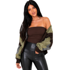 A woman modeling a brown strapless tube top, black faux-leather pants, and a chunky knit cardigan with olive green, brown, and gray color-blocked sleeves, set against a plain white background.