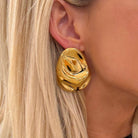 Gold earrings worn by a person with blonde hair.