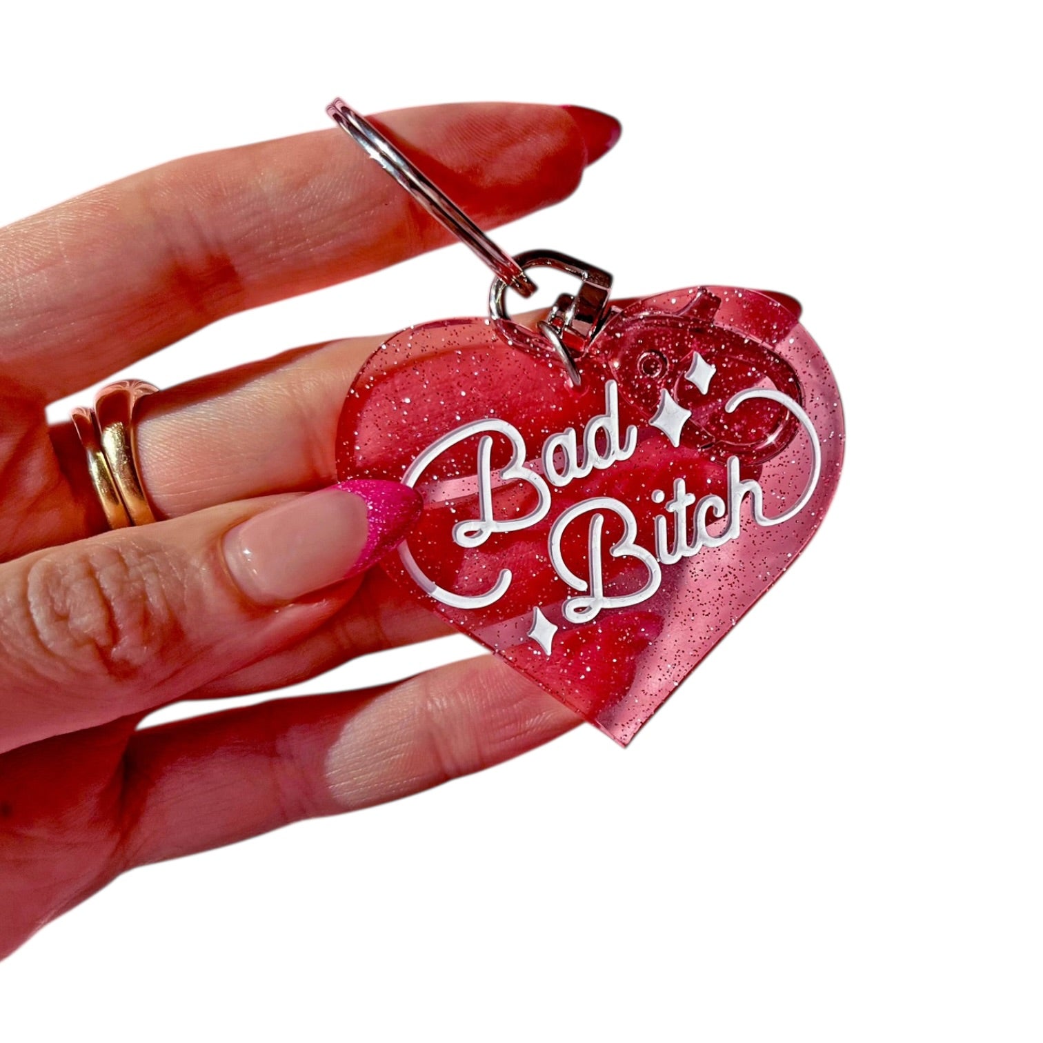 Pink glittery heart-shaped keychain with 'Bad Bitch' text held by a hand.