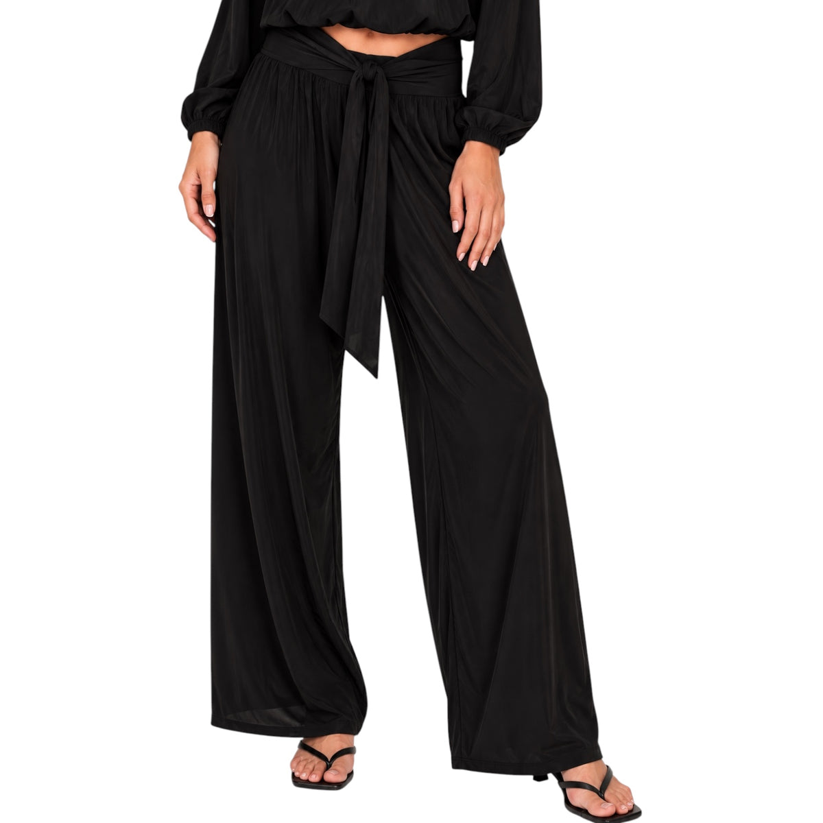 A model wearing black wide-leg draped pants with a matching waist tie, paired with black sandals against a plain white background.