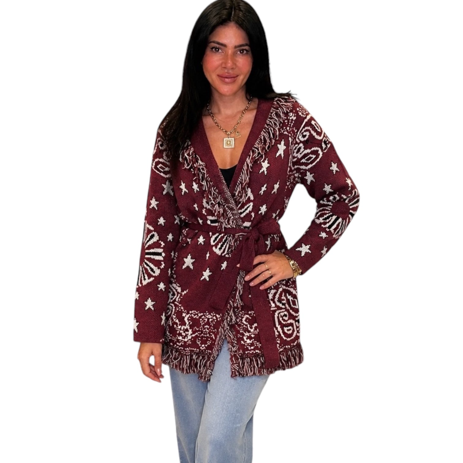 A woman modeling a long-sleeve wrap-style cardigan with a white star and paisley pattern on a burgundy base, paired with light blue jeans against a plain white background.