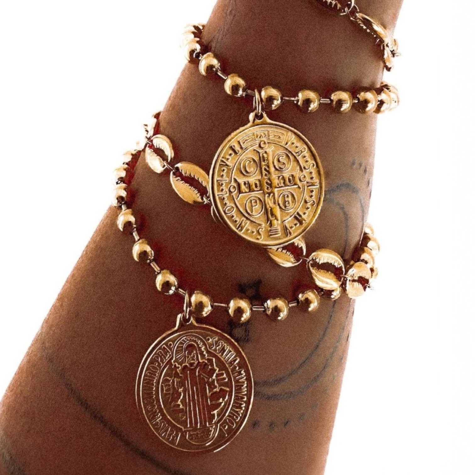 Gold bracelet with Saint Benedict medallions on a wrist against a white background