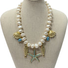 A pearl and gold statement necklace with seashell, starfish, and fish charms, displayed on a beige fabric jewelry bust.
