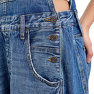 Close-up of a pair of blue denim shorts showing the back pocket, button details, and a person's hand and hip area.
