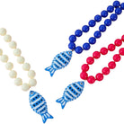 Three beaded necklaces on a white background: one with cream beads, one with bright blue beads, and one with bright red beads. Each necklace features a blue and white striped fish-shaped pendant.