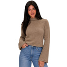 A woman modeling a cropped, long-sleeve knit sweater in a warm taupe-brown color, paired with blue jeans, against a plain white background.