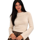A woman with long dark hair wearing a cream-colored, long-sleeve knit sweater and a brown patterned skirt, photographed against a solid white background.