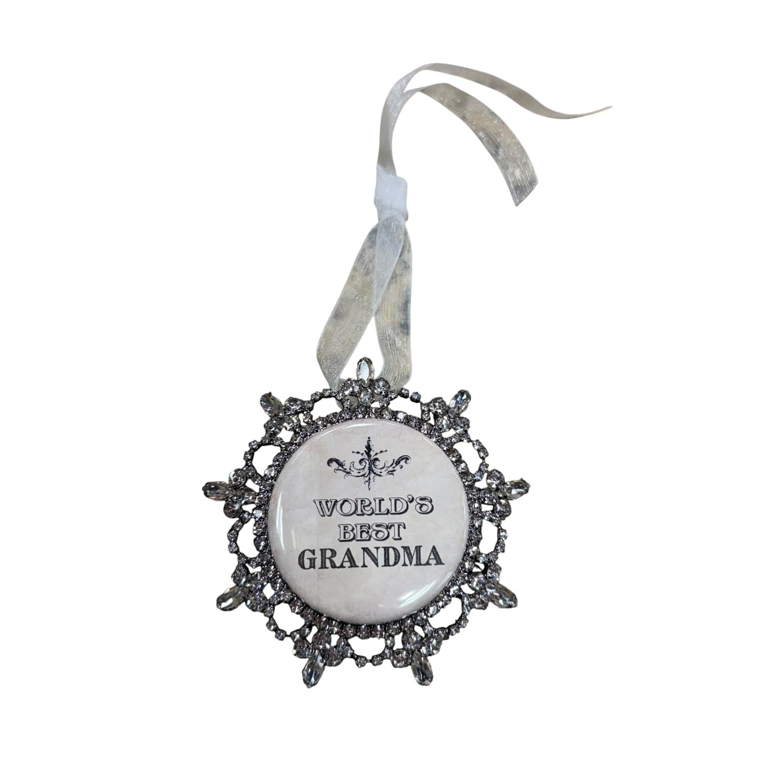 A decorative ornament featuring a circular white center with the text 'WORLD'S BEST GRANDMA' and a silver filigree border, hanging from a sheer silver ribbon on a white background.