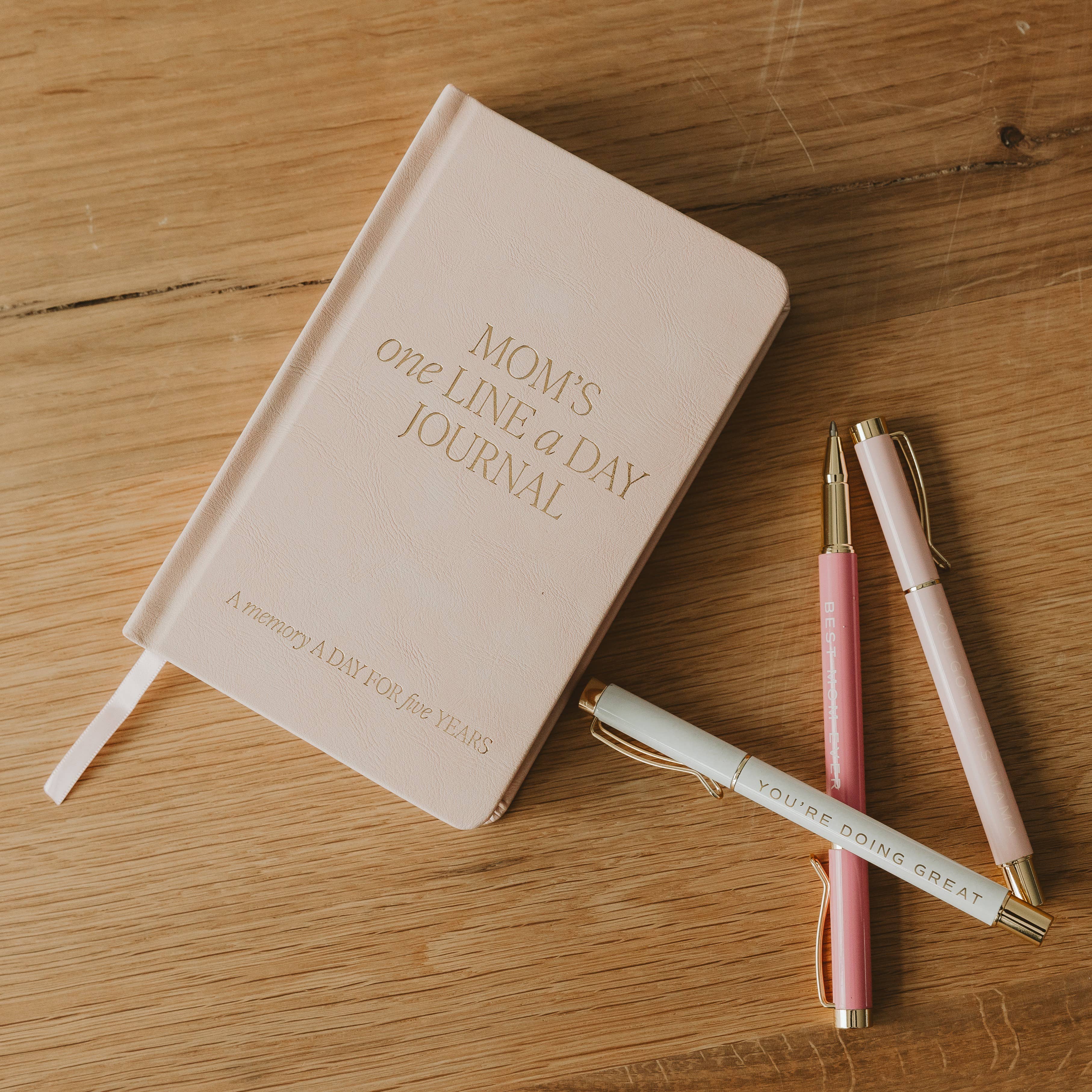 Journal titled 'Mom's One Line a Day Journal' with two pens on a wooden surface