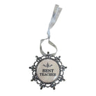 A decorative hanging ornament with a round cream center that reads “BEST TEACHER” in black text, surrounded by an ornate dark silver filigree border and a white ribbon loop at the top.
