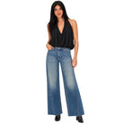 A woman modeling a black sleeveless halter top and wide-leg blue jeans against a plain white background.
