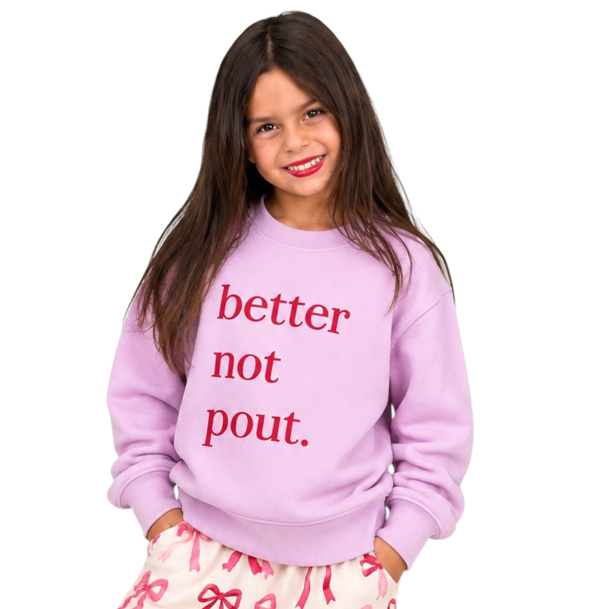 A young girl with long brown hair smiling, wearing a light purple sweatshirt with the text 'better not pout.' in red, paired with pink patterned pants, against a solid white background.