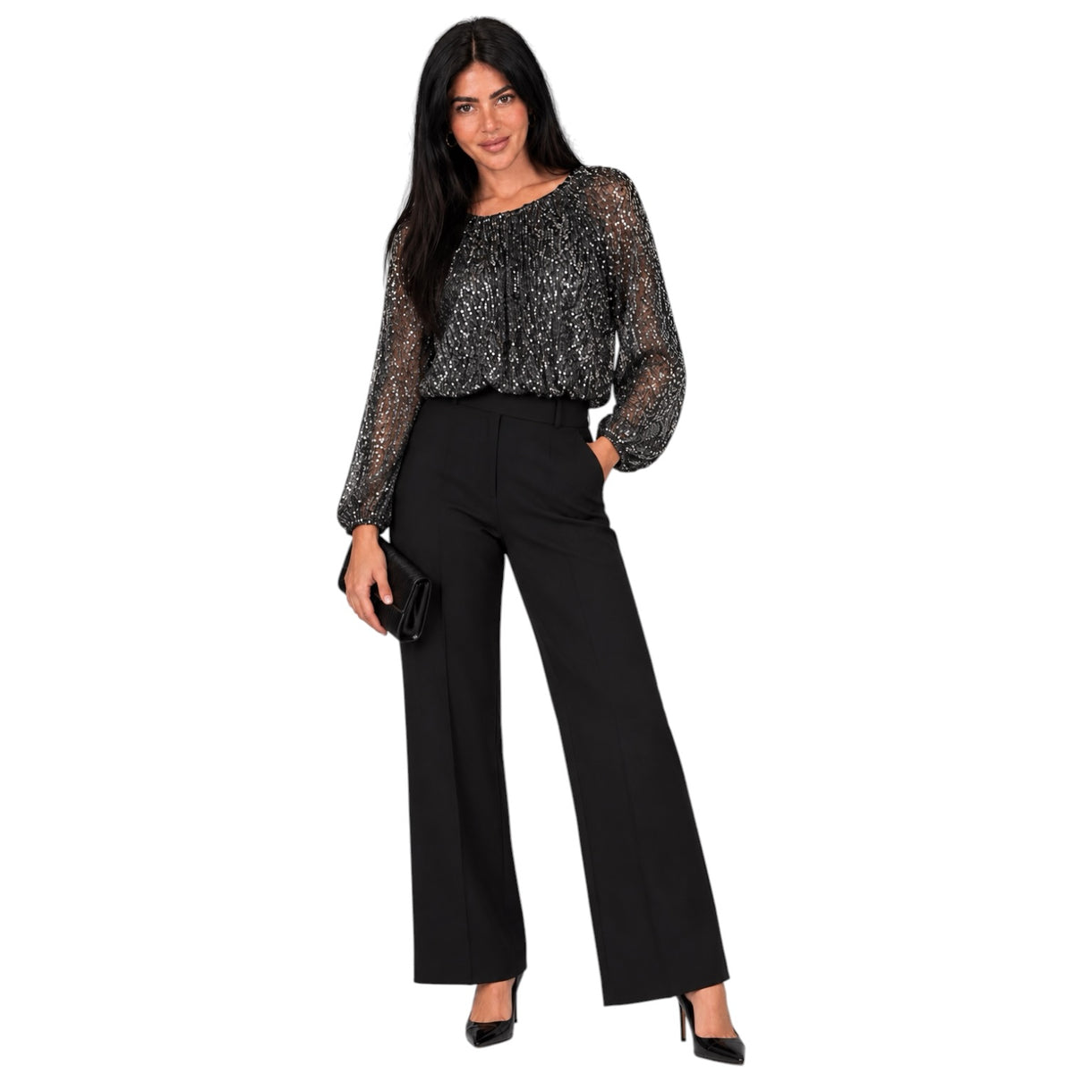 A woman modeling a black and silver glittery sheer long-sleeve top paired with black wide-leg trousers and black heels, standing against a plain white background.