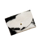 A small black and white cowhide cardholder with a gold snap button, shown on a plain white background.