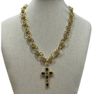 Gold chain necklace with a cross pendant featuring black stones, displayed on a beige fabric mannequin bust against a white background.