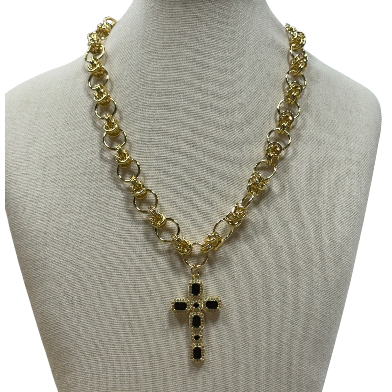 Gold chain necklace with a cross pendant featuring black stones, displayed on a beige fabric mannequin bust against a white background.