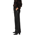 A model shown from the waist down wearing black wide-leg faux leather trousers with side slits, paired with a brown and black argyle sweater and black pointed-toe heels, against a plain white background.