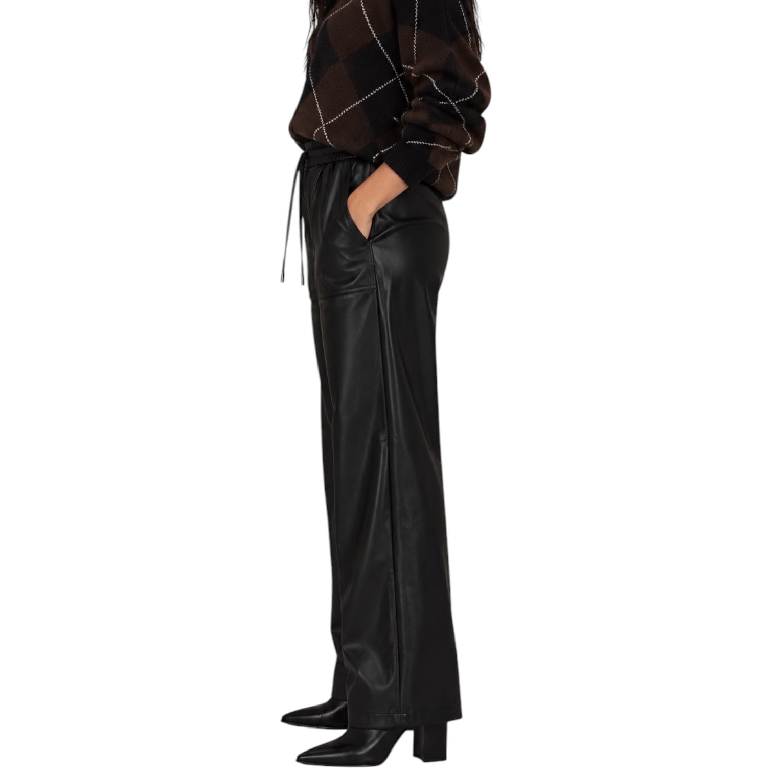A model shown from the waist down wearing black wide-leg faux leather trousers with side slits, paired with a brown and black argyle sweater and black pointed-toe heels, against a plain white background.