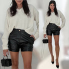 Woman wearing a white sweater and black leather shorts with a small black handbag.