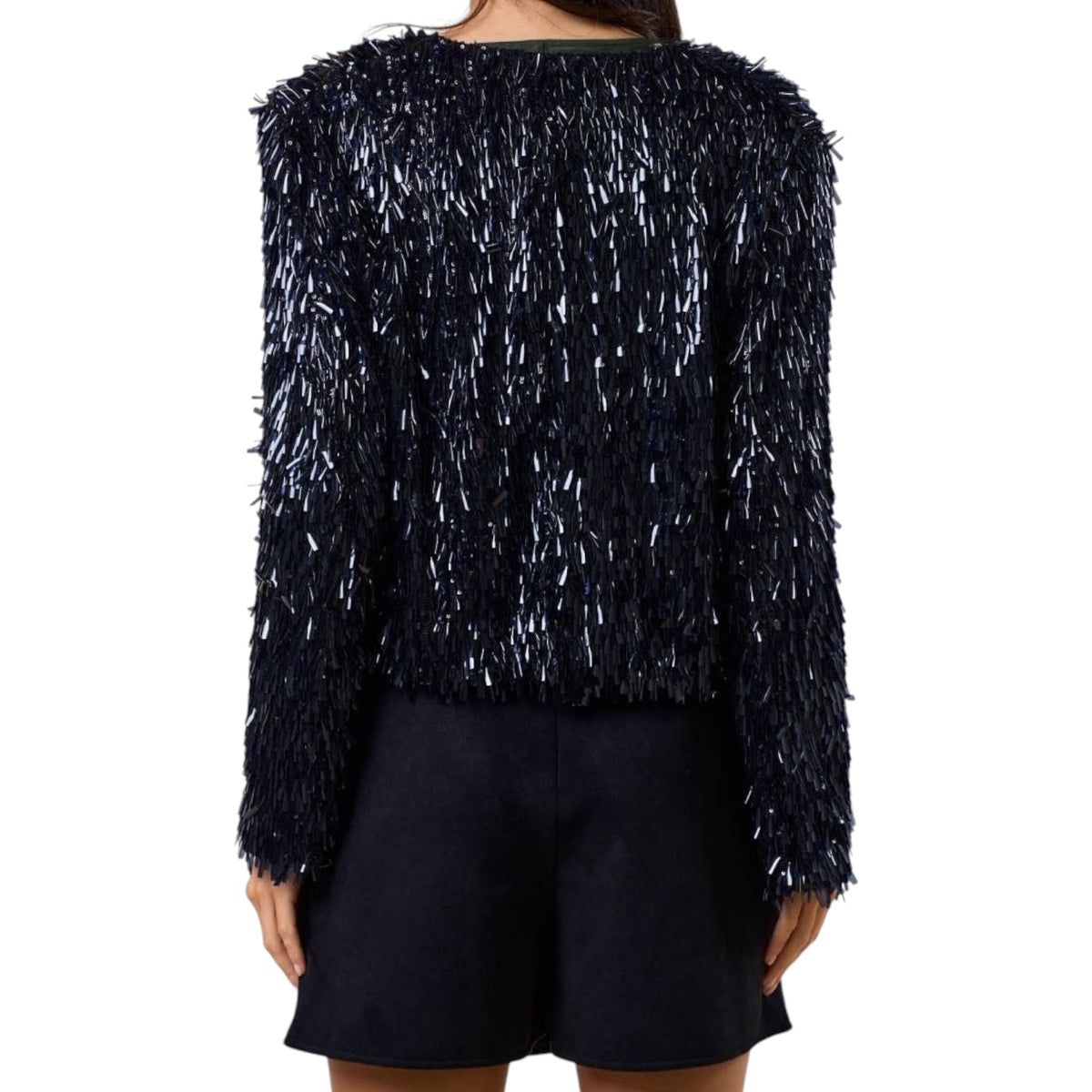 A model shown from the back wearing a long-sleeve, dark navy blue textured jacket covered in dense, shimmery silver and white fringe, paired with dark shorts against a plain white background.