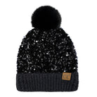 A black beanie hat covered in sequins, featuring a fluffy black pom-pom on top and a dark ribbed cuff with a small tan leather patch showing the letters 'CC'.