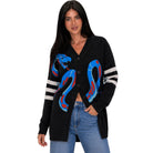 A woman modeling a black knit cardigan with a large blue and red snake graphic on the front and white stripes on the sleeves, paired with blue jeans against a plain white background.