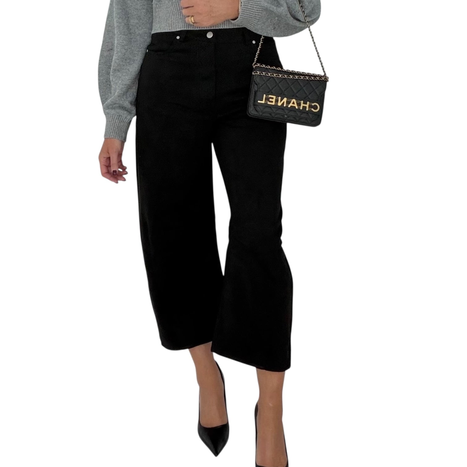 Person wearing black suede barrel pant and holding a Chanel handbag on a white background