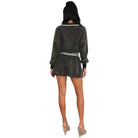 A woman shown from the back wearing a dark gray textured long-sleeve romper with a white collar and a ruffled waistband, paired with beige high heels against a plain white background.