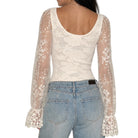 A woman shown from the back wearing a cream lace long-sleeve scoop-neck top with sheer floral lace sleeves and light-wash blue jeans against a plain white background.