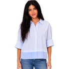 A woman modeling a light blue and white vertically striped button-down shirt with rolled-up sleeves and a matching striped hem detail, paired with blue jeans against a plain white background.