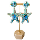 Starfish-shaped earrings with turquoise and blue beads on a gold stand against a white background