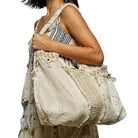 Woman holding a large, intricately designed beige bag against a white background