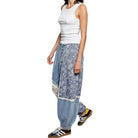 Person wearing a white tank top and blue patterned harem pants on a white background
