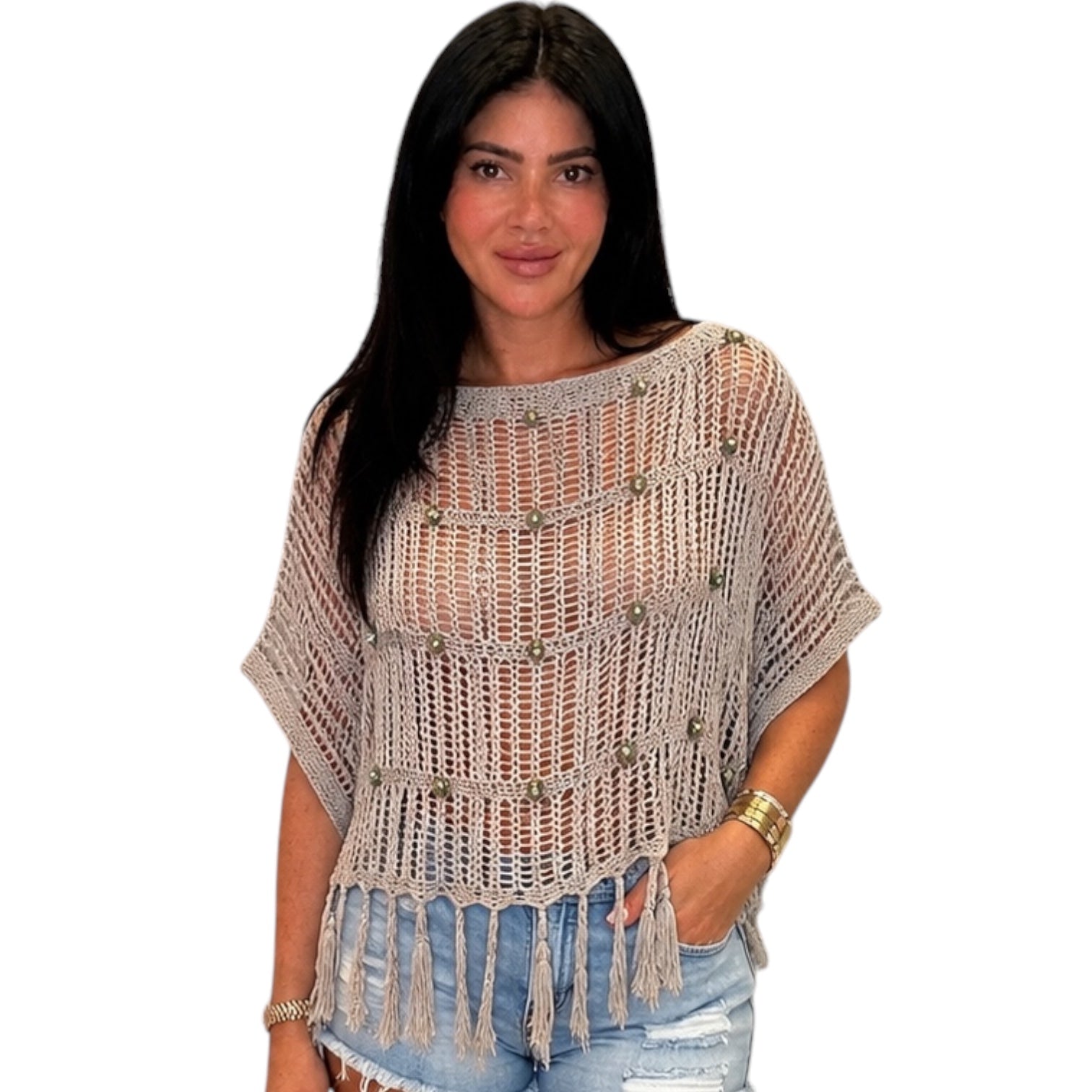 Woman wearing a beige crochet poncho with tassels on a white background
