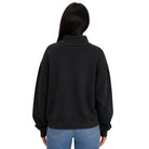 A woman viewed from the back wearing a black long-sleeve sweatshirt with a mock neck and ribbed cuffs, paired with blue jeans, against a plain white background.