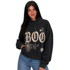 A woman wearing a black crewneck sweatshirt with a distressed cream graphic that reads 'BOO' decorated with spiderwebs and spiders, paired with blue jeans against a plain white background.
