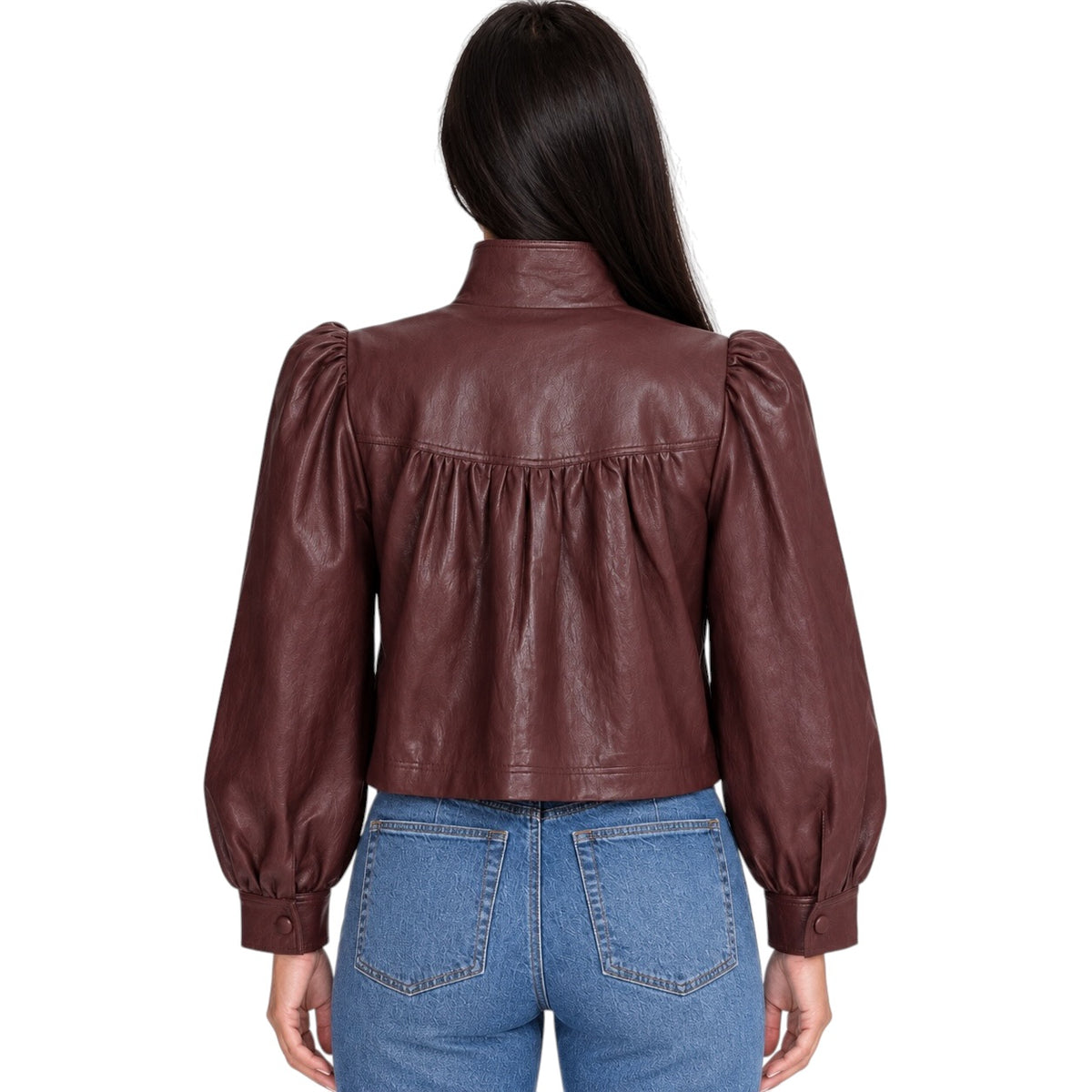 A woman viewed from the back wearing a dark brown faux-leather cropped jacket with puffed long sleeves and gathered detailing at the back, paired with blue jeans, against a plain white background.