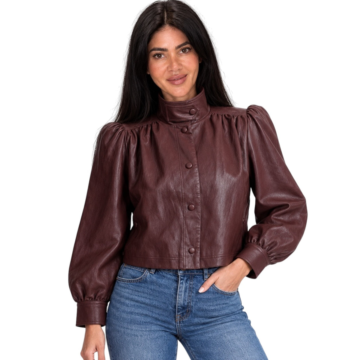 A woman modeling a dark brown faux leather jacket with a high mock neck, button front, and puffed balloon sleeves, paired with blue jeans against a plain white background.