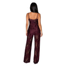 A woman viewed from the back wearing a burgundy satin jumpsuit with floral lace detailing on the bodice and wide legs, set against a plain white background.