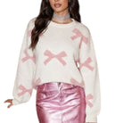 White sweater with pink bows worn by a model on a white background