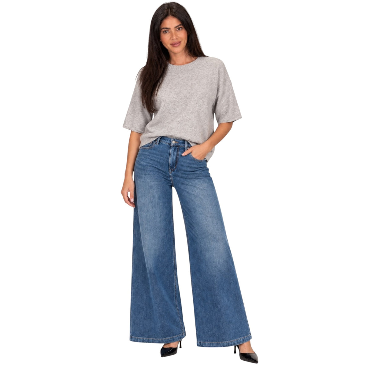 A woman modeling a light gray short-sleeve knit top and wide-leg blue denim jeans with black pointed-toe heels, set against a plain white background.