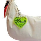 Green heart-shaped keychain with 'Brat' text on a beige bag.