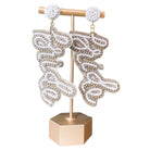 Pair of bride-shaped earrings on a gold stand with a white background
