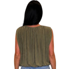 A woman viewed from the back wearing a sleeveless olive green top with a gathered, pleated back design and light blue jeans, set against a plain white background.