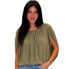 A woman wearing an olive green draped short-sleeve top with side cutouts, paired with blue jeans, against a plain white background.