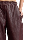 Close-up of a person wearing dark brown textured wide-leg pants with an elastic waistband and side pocket, shown against a plain white background.
